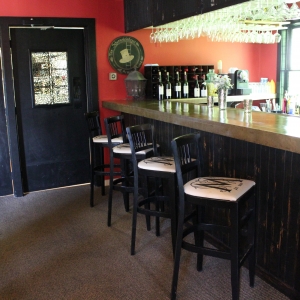 full bar with high top chairs and glasses hanging from above